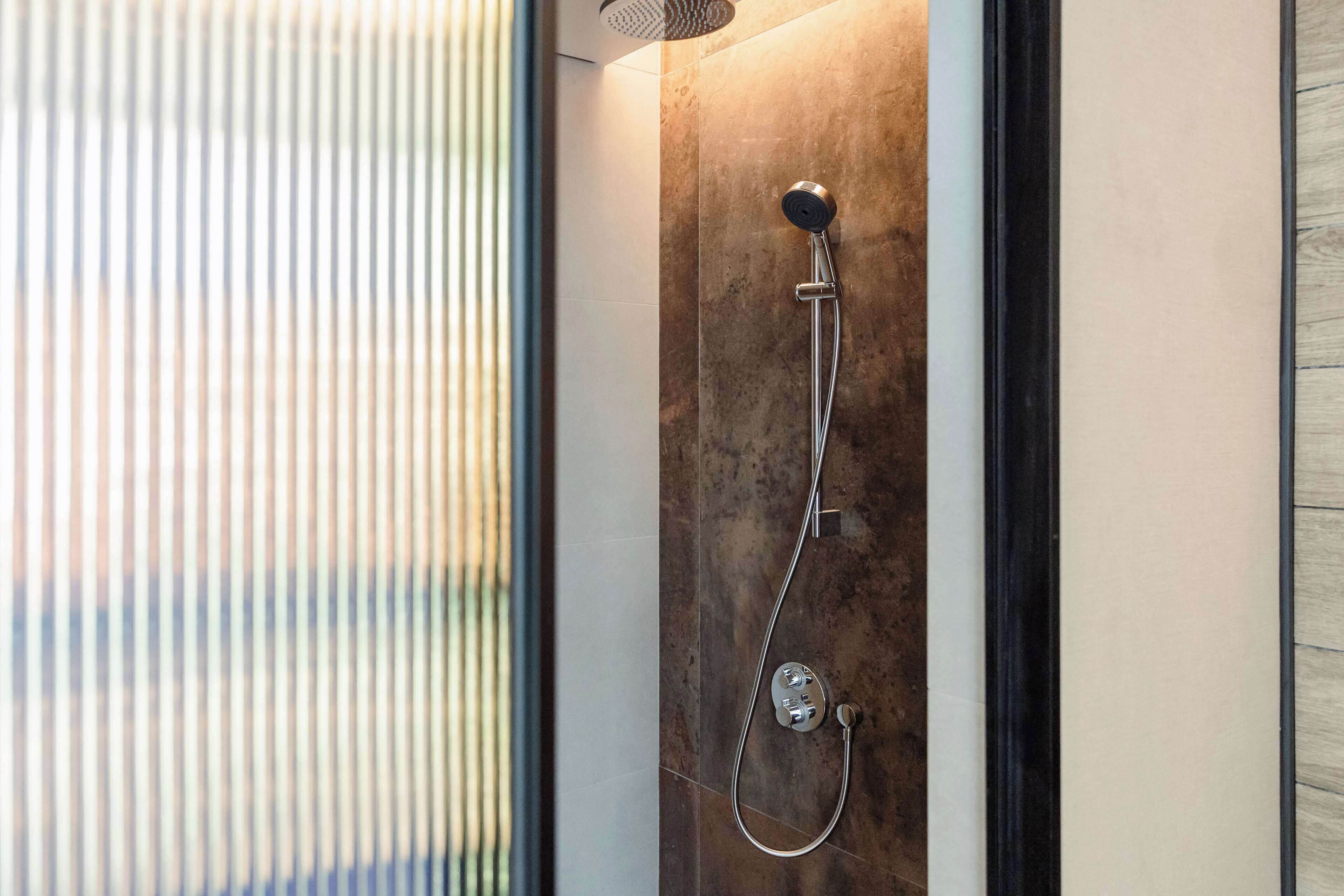 A modern shower with a handheld showerhead and a wall-mounted control panel.