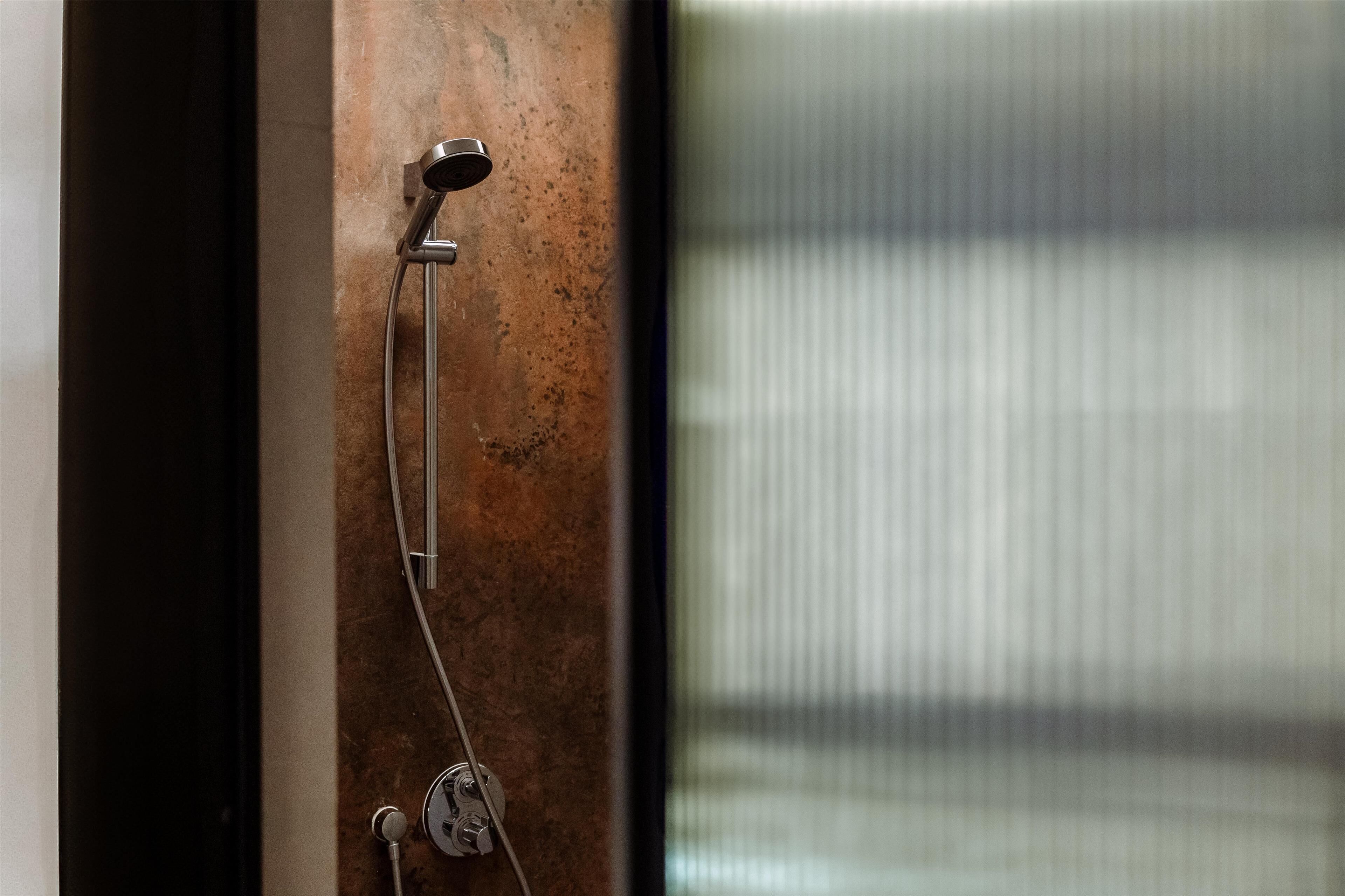 Une douche dotée d’un pommeau métallique et d’une molette de réglage, le tout fixé sur un mur à texture.
