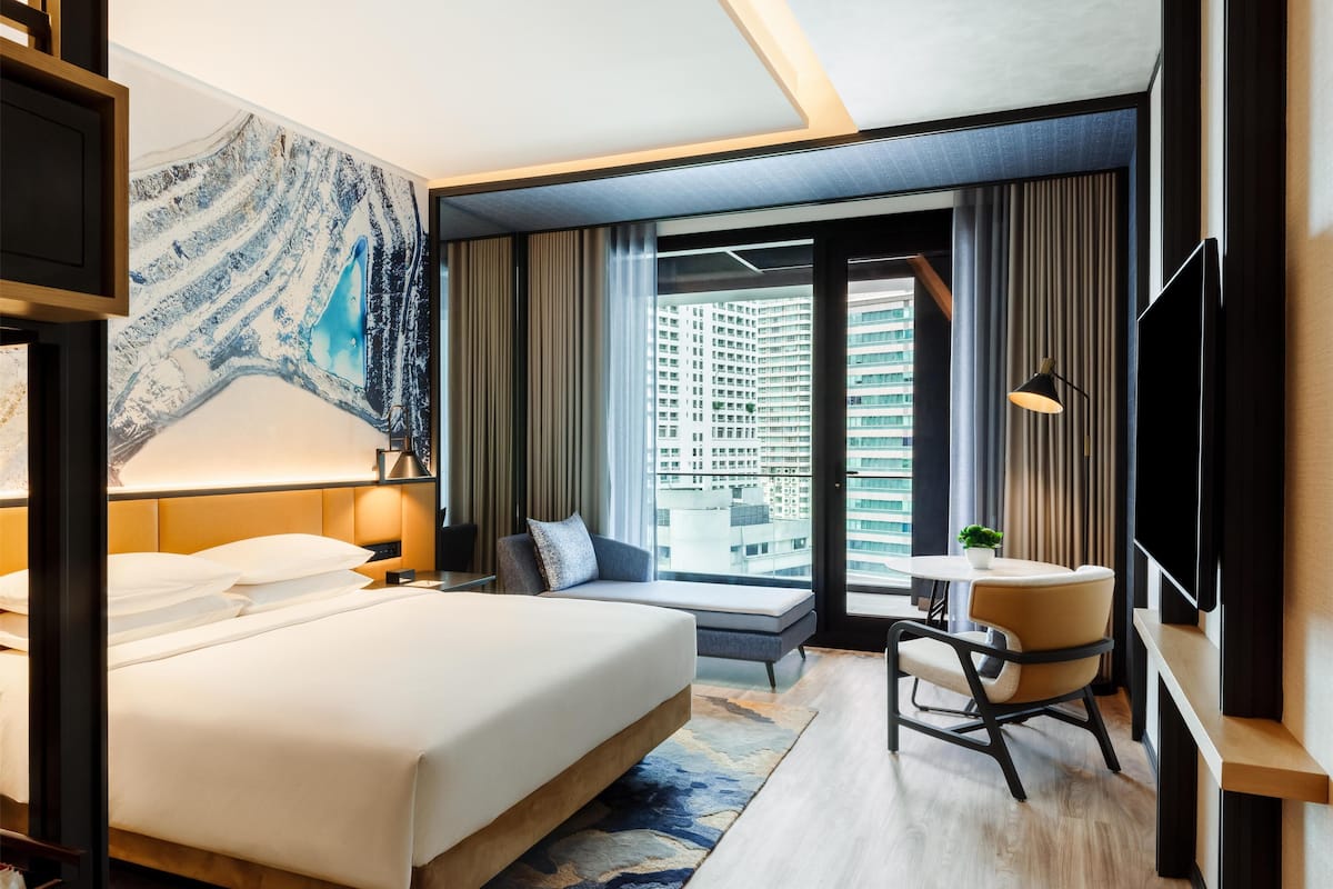 A modern hotel room with a large bed, a seating area with a view of the city, and a flat-screen TV.