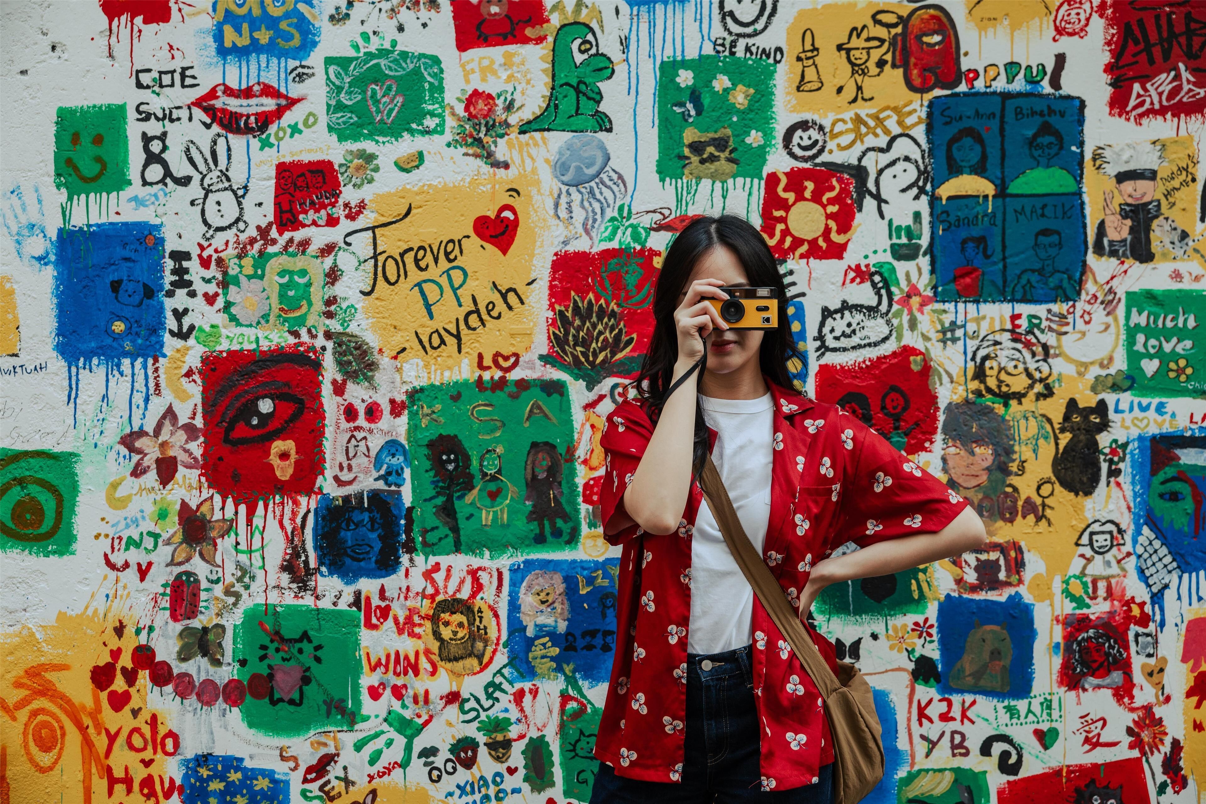 A person taking a photo with a camera against a colorful graffiti wall.