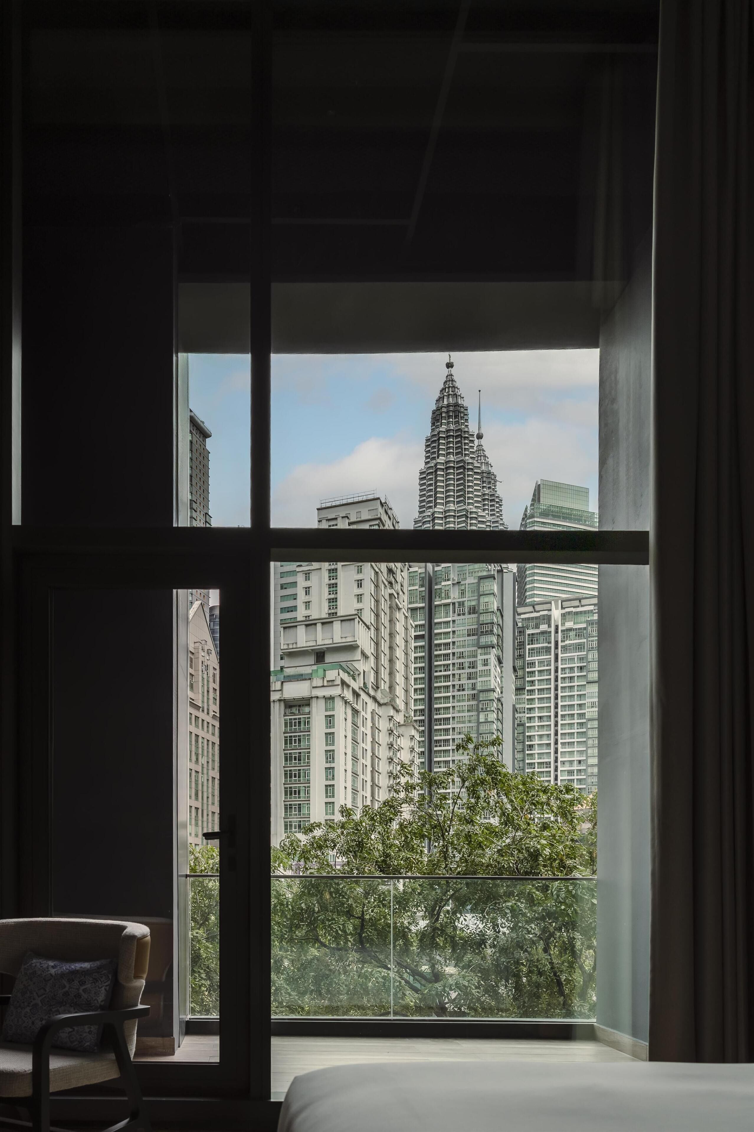 Une chambre d’hôtel moderne dotée d’une grande fenêtre donnant sur des immeubles de grande hauteur et sur un paysage verdoyant.