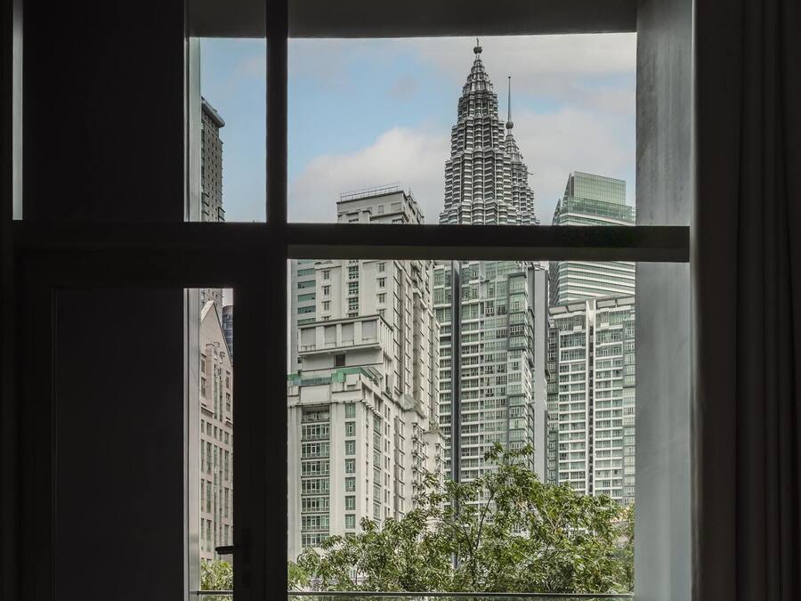 A modern hotel room with a large window offering a view of high-rise buildings and greenery.