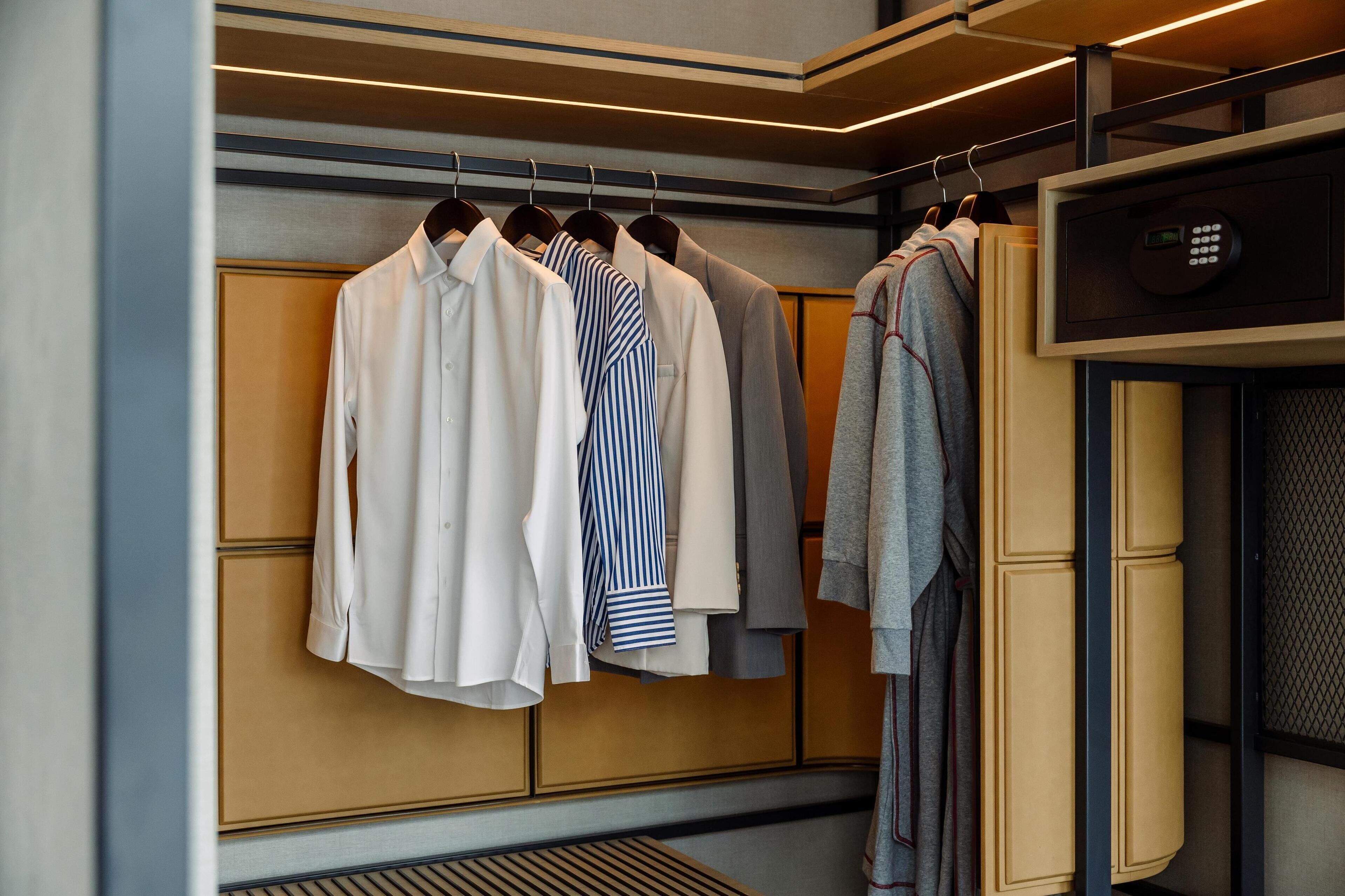 A hotel room with a wardrobe containing neatly hung shirts and a robe.