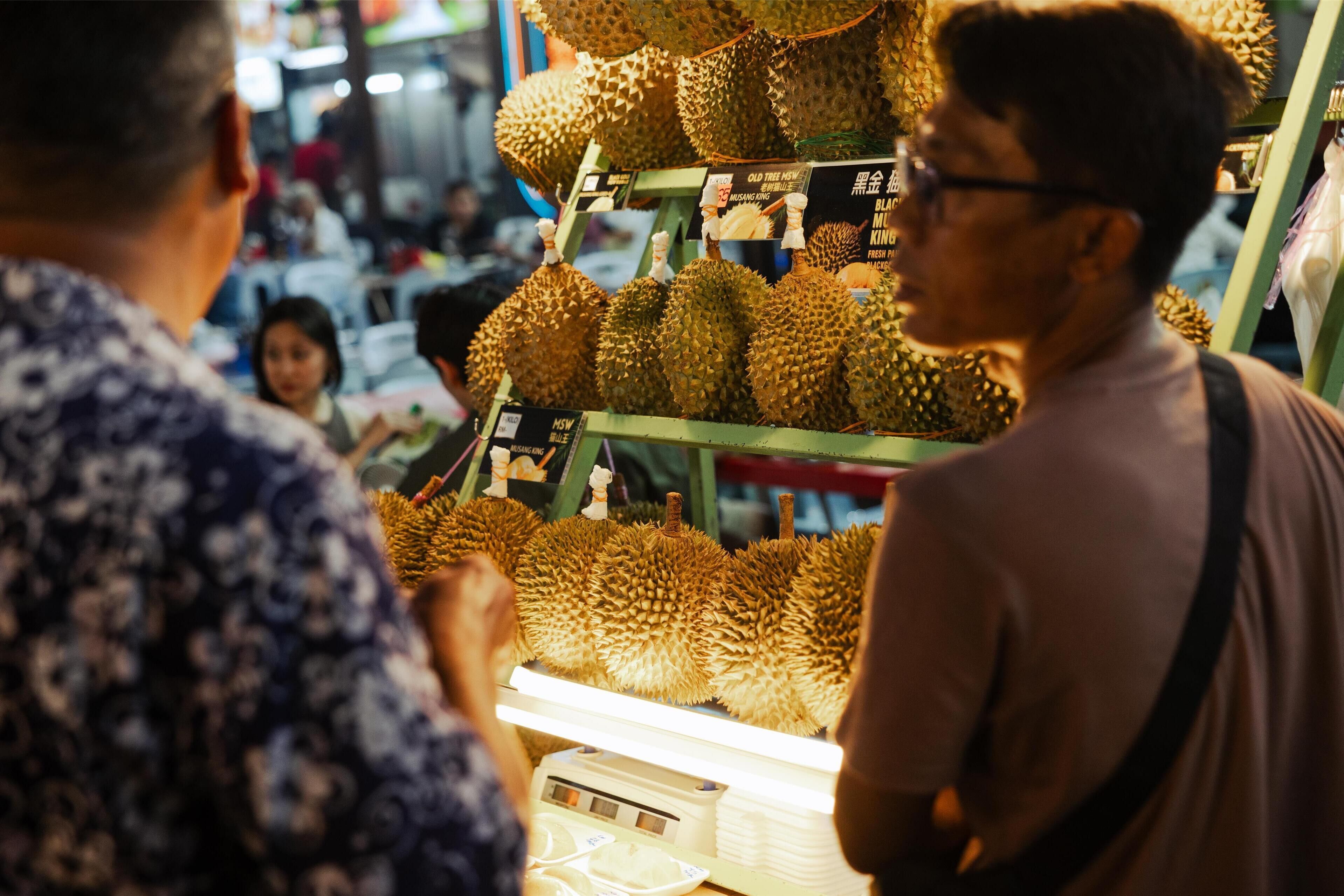 A durian fruit display in a market with a price sign and a weighing scale.