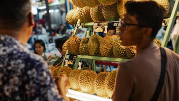 Exhibición de durios en un mercado, con un cartel de precios y una balanza.