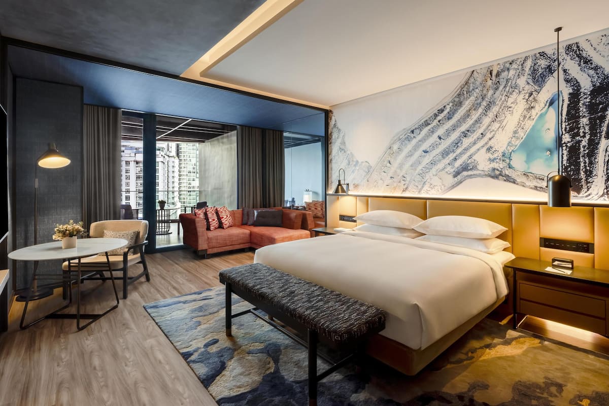 A modern hotel room with a large bed, a seating area with a sofa and chairs, a small table, and a large wall mural.
