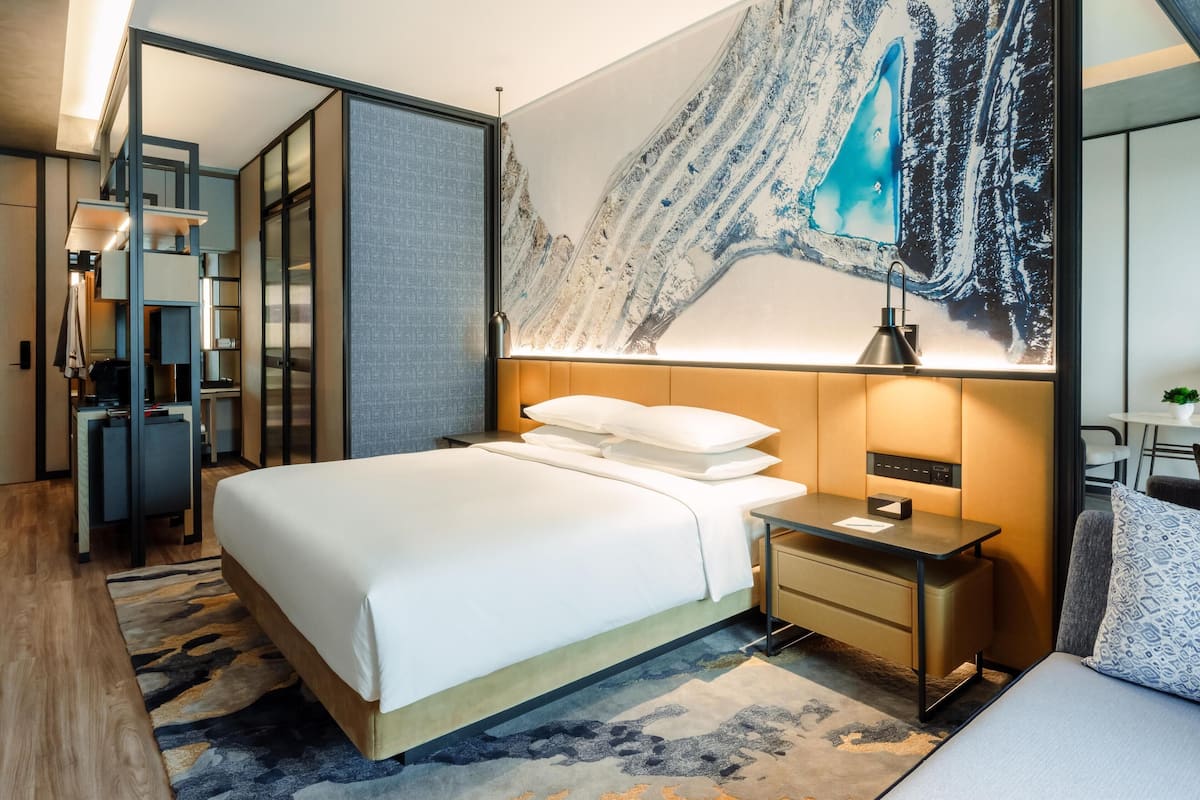 A modern hotel room with a large bed, a desk, and a large painting on the wall.