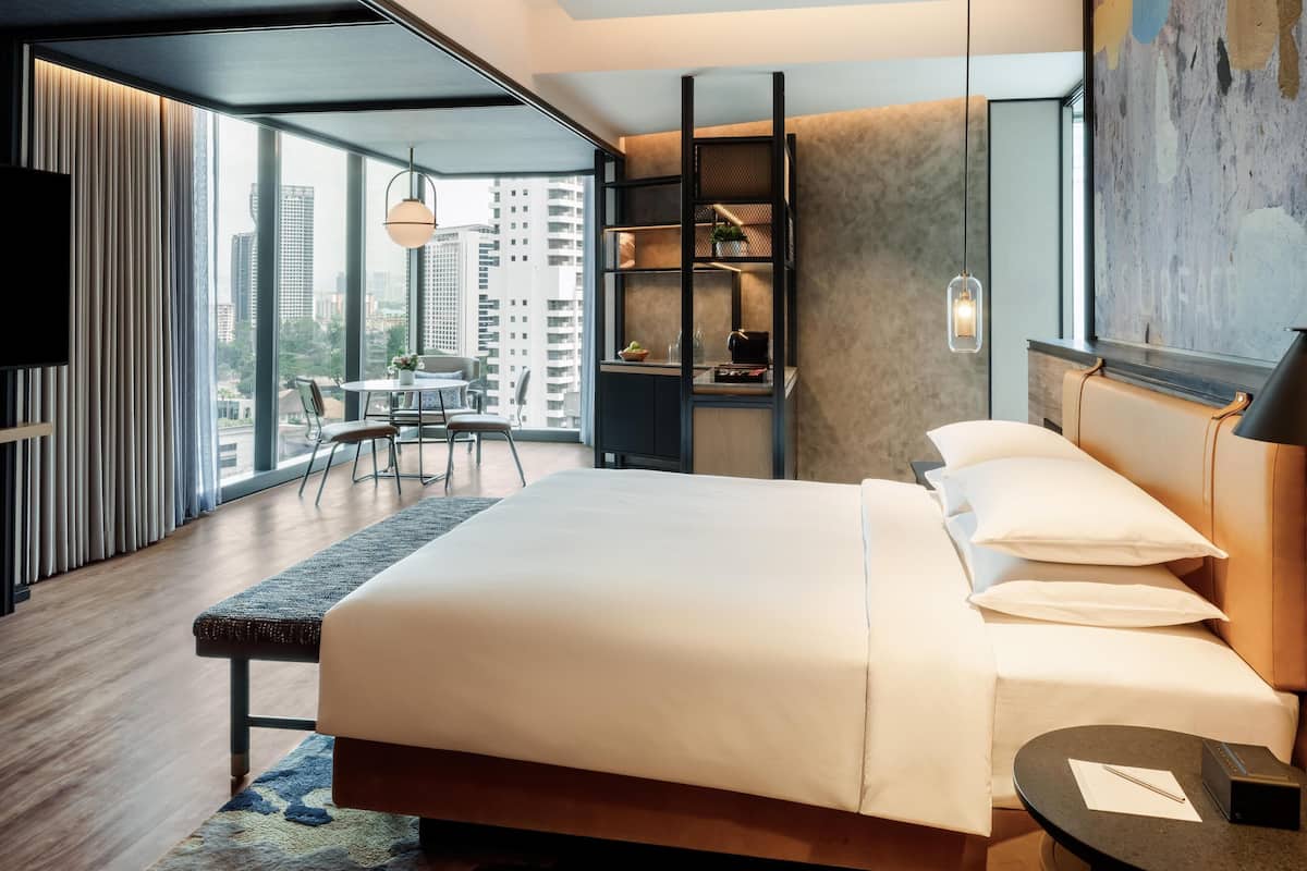 A modern hotel room with a large bed, a desk, and a view of the cityscape.
