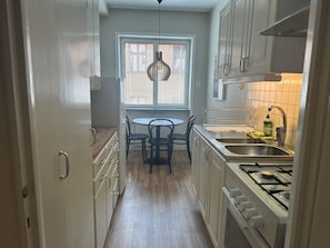 Uma cozinha com uma mesa de jantar, cadeiras, fogão a gás e uma janela com persianas.