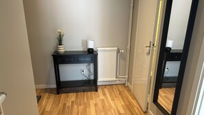A room with a wooden floor, a black console table with drawers, a white radiator, and a door with a black frame.