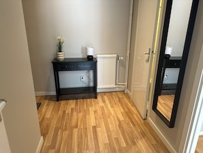 Quarto com piso de madeira, mesa de console preta com gavetas, radiador branco e porta com moldura preta.