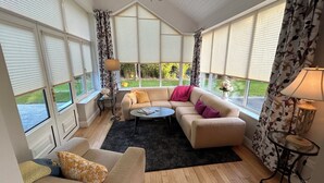 A cozy living room with a sectional sofa, a round coffee table, and a chandelier. Large windows with blinds provide ample natural light. - 4 bedroom detached home close to Kenmare town (Kenmare)