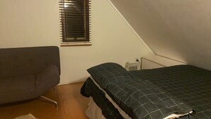 Pieni, kolmionmuotoinen huone, jossa on sänky, tuoli ja patteri.