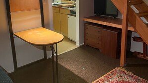 Pieni huone, jossa on sänky, tuoli, työpöytä, televisio ja portaat.