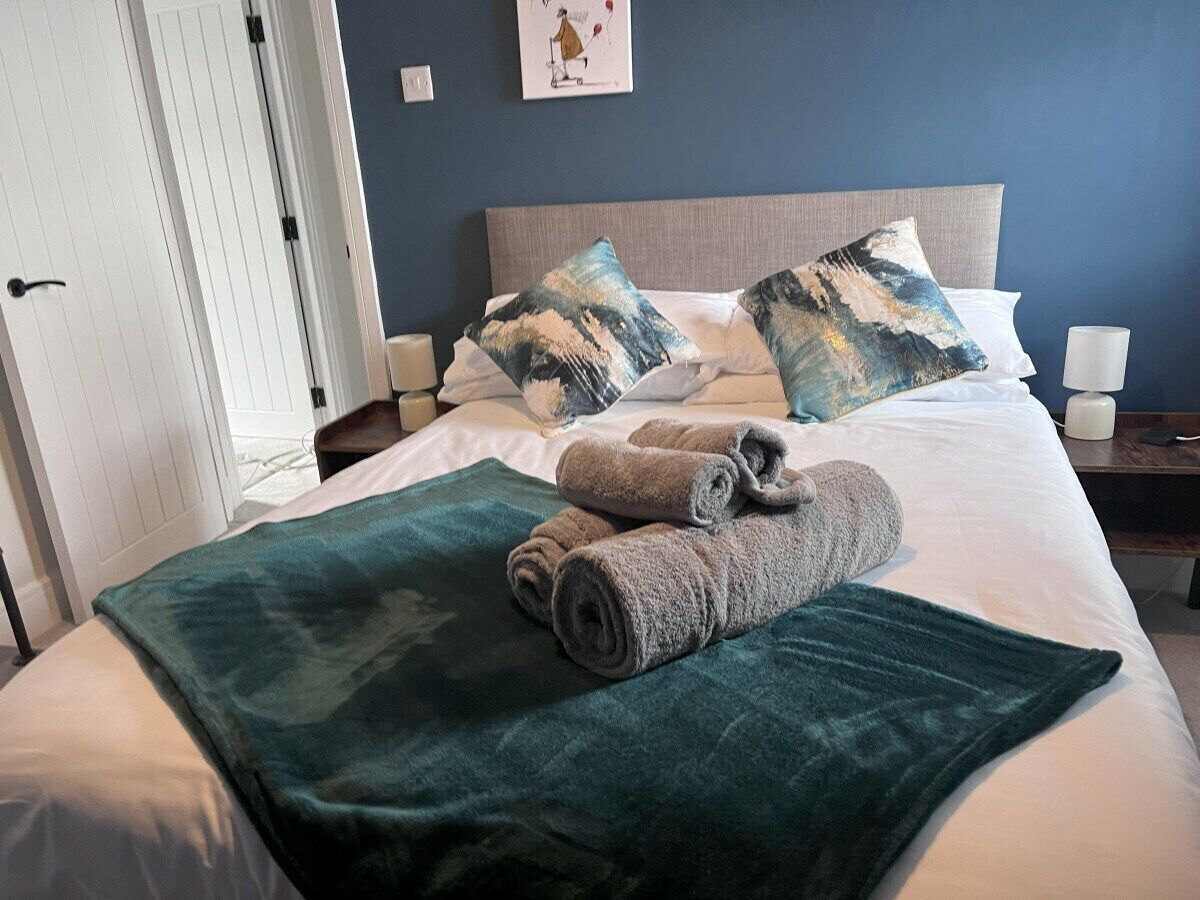 Habitación de hotel con una cama, dos almohadas, una mesita de noche con lámpara y una puerta.