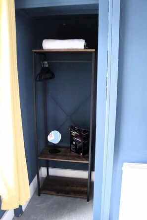 Un pasillo estrecho con un mueble de madera oscura contra una pared azul, que contiene una toalla blanca, un espejo y algunas cajas.