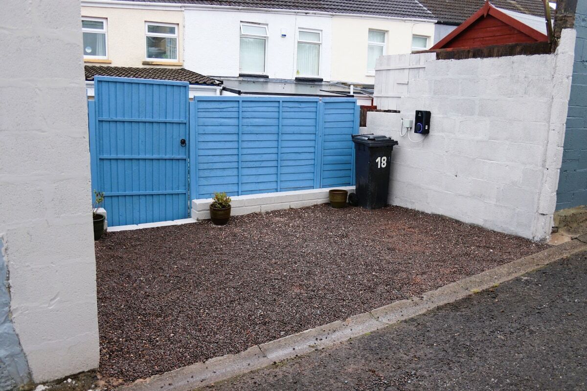A gated area with a blue gate, a black trash bin, and a white wall with a number plate.