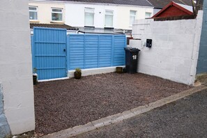 A gated area with a blue gate, a black trash bin, and a white wall with a number plate.