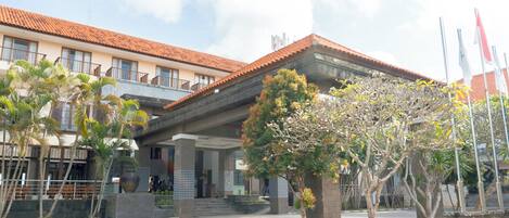A building with a red-tiled roof, a covered entrance, and a small garden area with trees and a large planter.