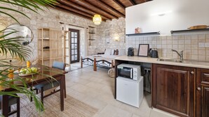 A cozy kitchen with a stone wall, wooden cabinets, and a built-in microwave. - Inia Lara Suites by Nomads (Paphos)