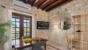 A dining area with a stone wall, wooden ceiling, and a table with chairs. There is a wall-mounted photo display and a floor lamp. - Inia Lara Suites by Nomads (Paphos)