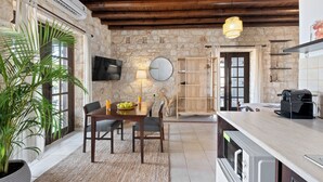 A rustic kitchen with stone walls, wooden beams, a dining area with a table and chairs, and a built-in oven. - Inia Lara Suites by Nomads (Paphos)
