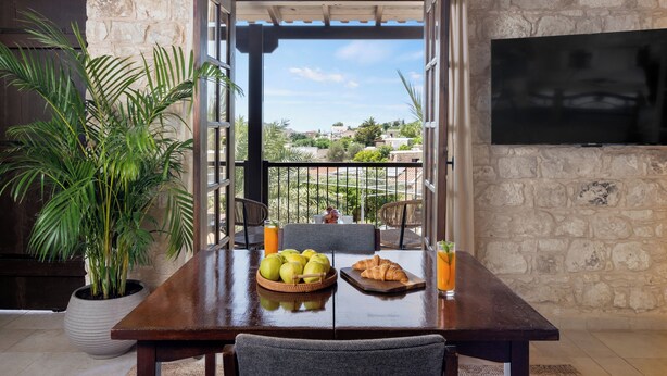 A dining table with a breakfast setting, including fruits, a croissant, and a glass of orange juice. - Inia Lara Suites by Nomads (Paphos)