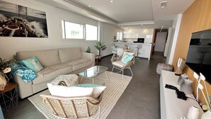 A modern living room with a sofa, a coffee table, and a dining area with chairs. - Clara Beach Blue Infinity (Cumbre del Sol)