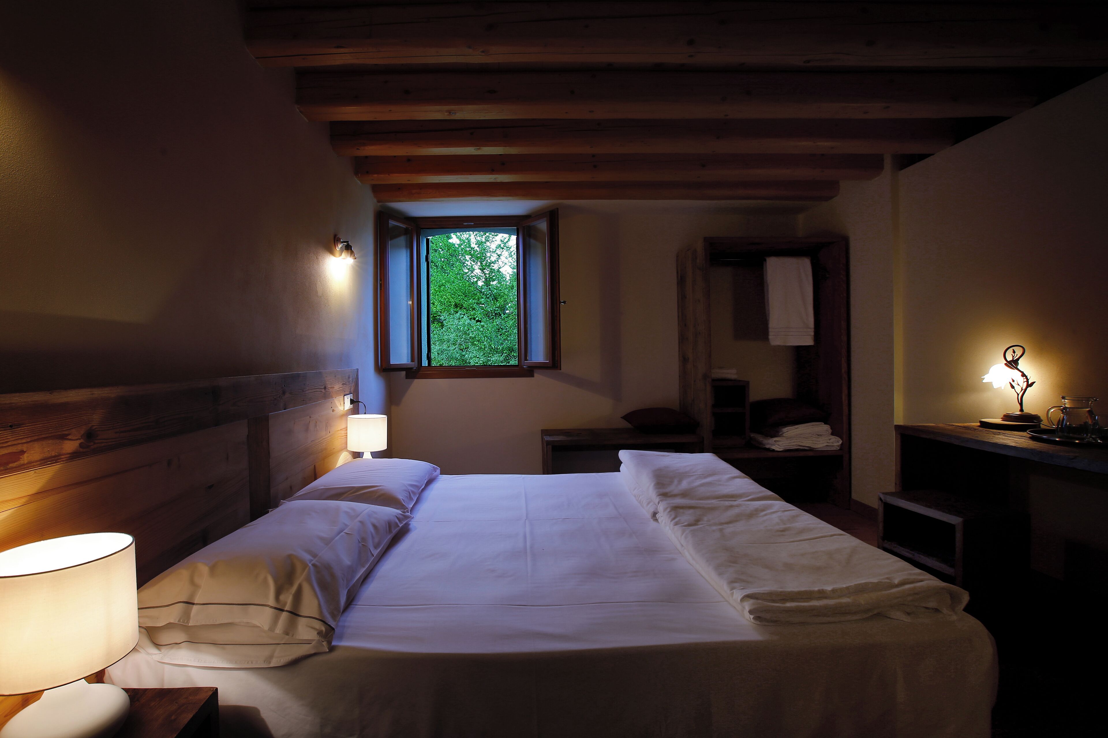 A room with a bed, a window, a nightstand, and a lamp.
