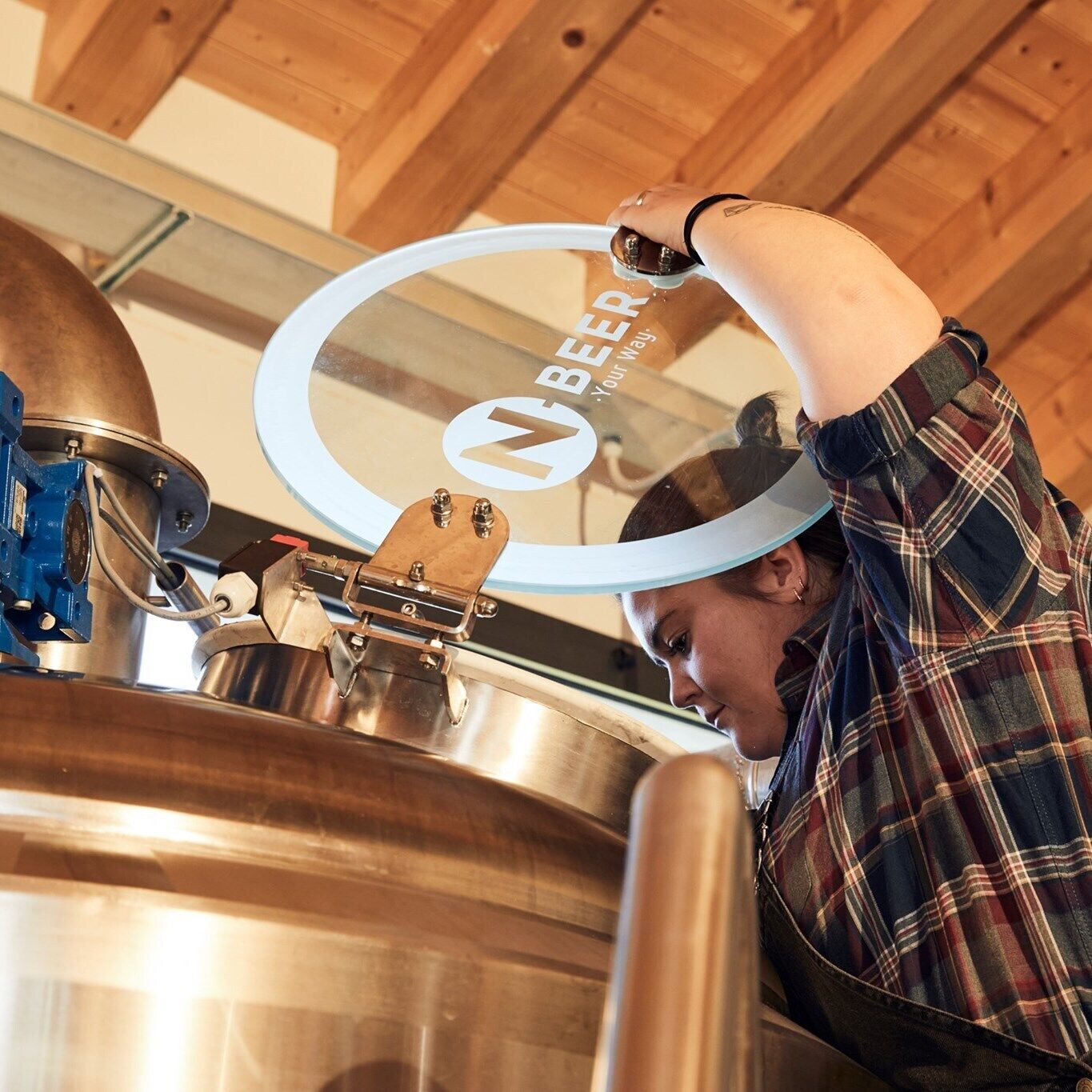 A person working with a large brewing kettle in a wooden interior.