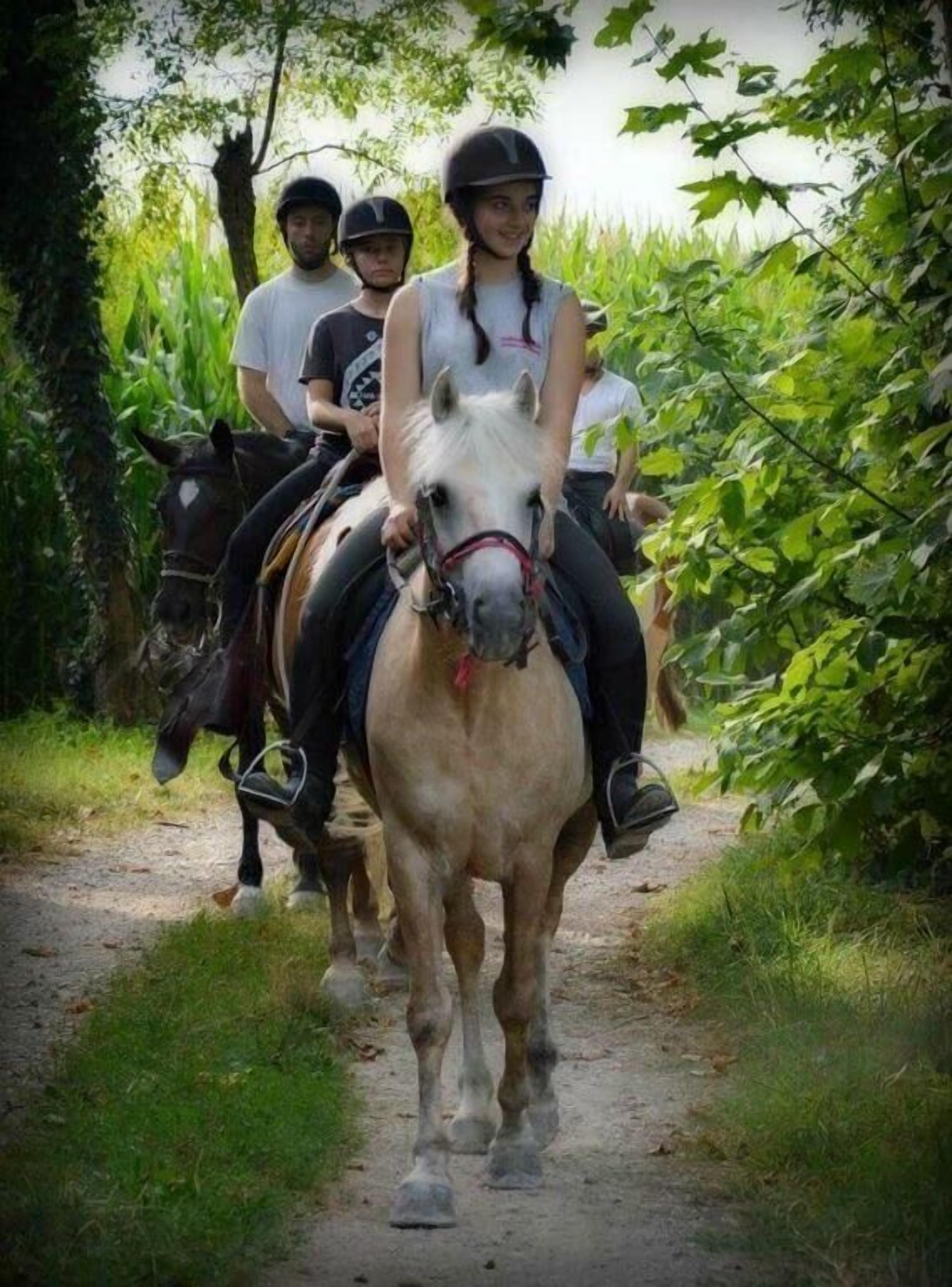 Tres personas cabalgando a caballo por un sendero estrecho rodeado de vegetación.