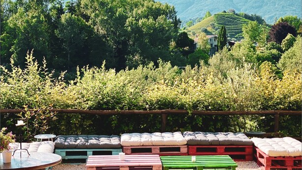 Une terrasse dotée de mobilier en bois, d’un tonneau et offrant une vue sur les montagnes et les vignobles.