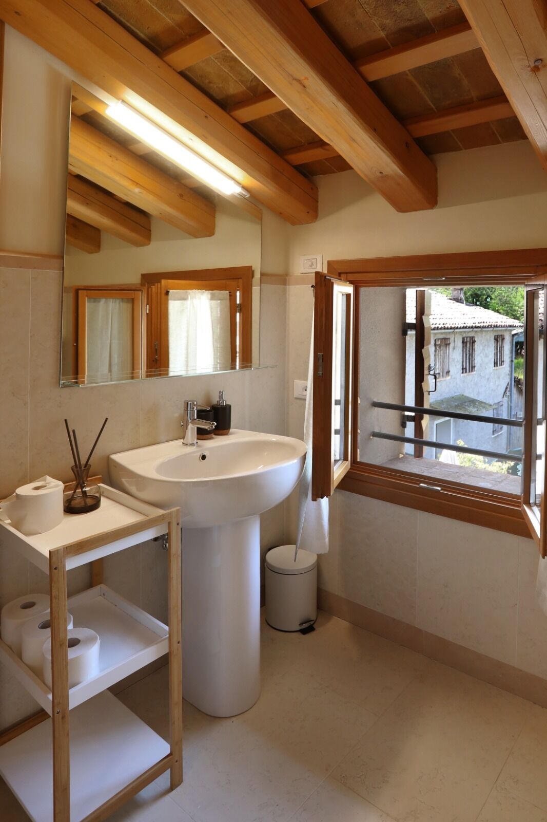 A bathroom with a wooden ceiling, a large sink, a mirror, and a window overlooking a building.