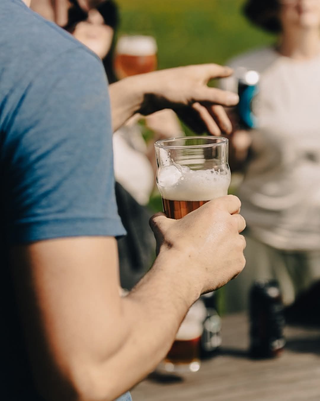 A person holding a glass of beer at a table with other people.