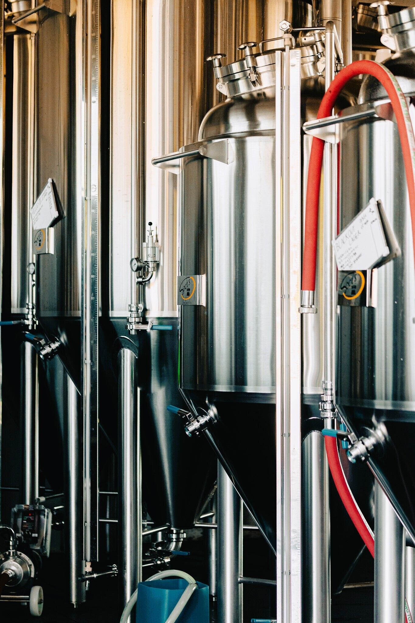 Tanques de elaboración de acero inoxidable con válvulas y mangueras, probablemente parte del sistema de producción de una cervecería.