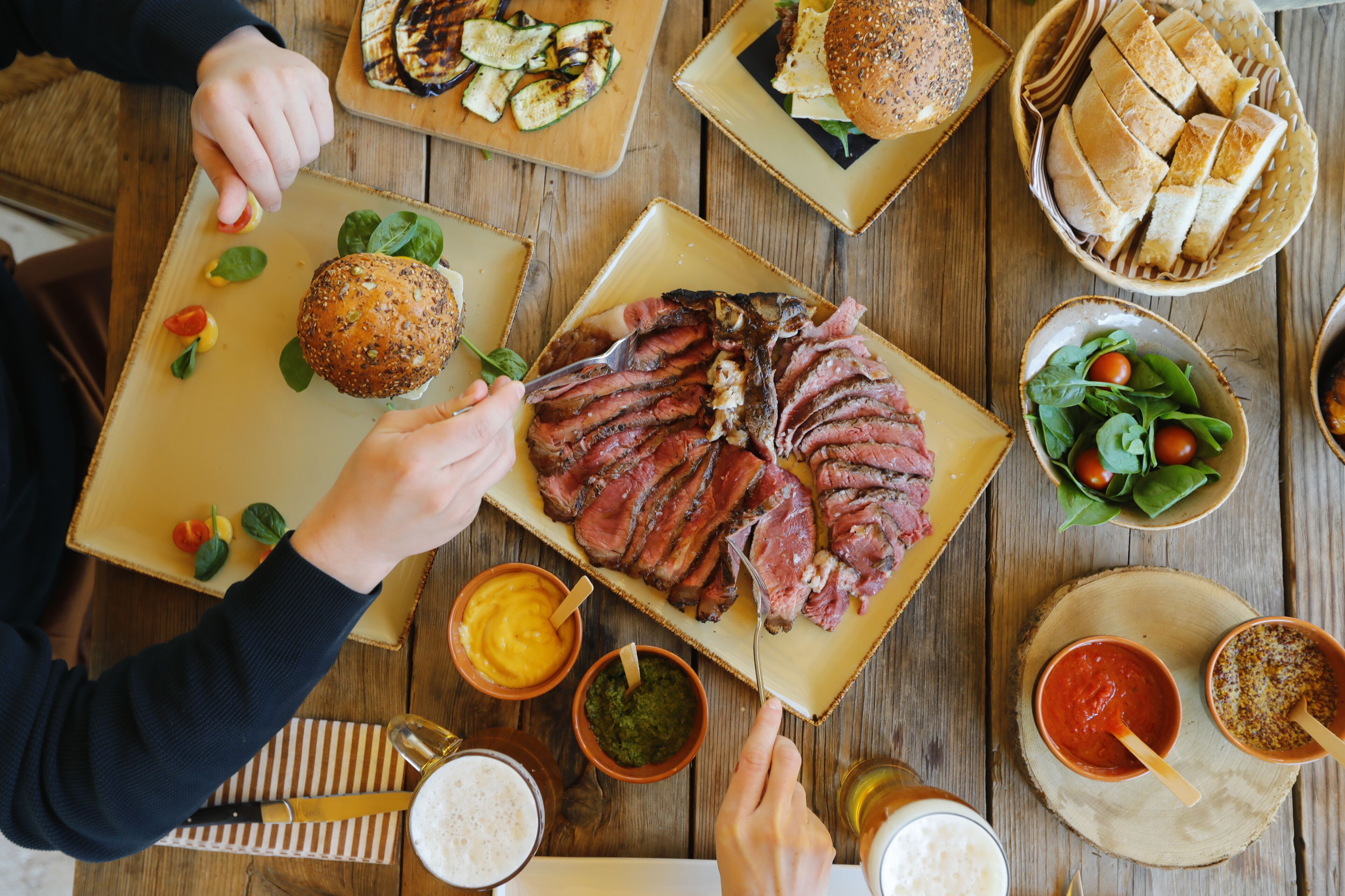 Un tavolo di legno con diversi cibi, tra cui salumi, pane e verdure.
