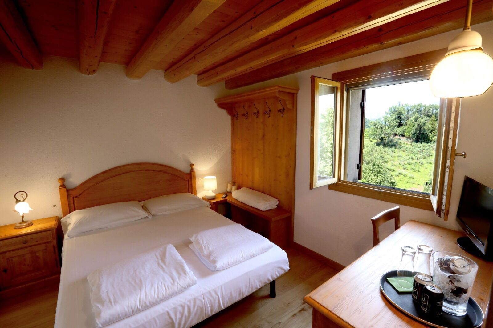 Una stanza in legno con un letto, un comodino e una finestra che si affaccia sul verde.