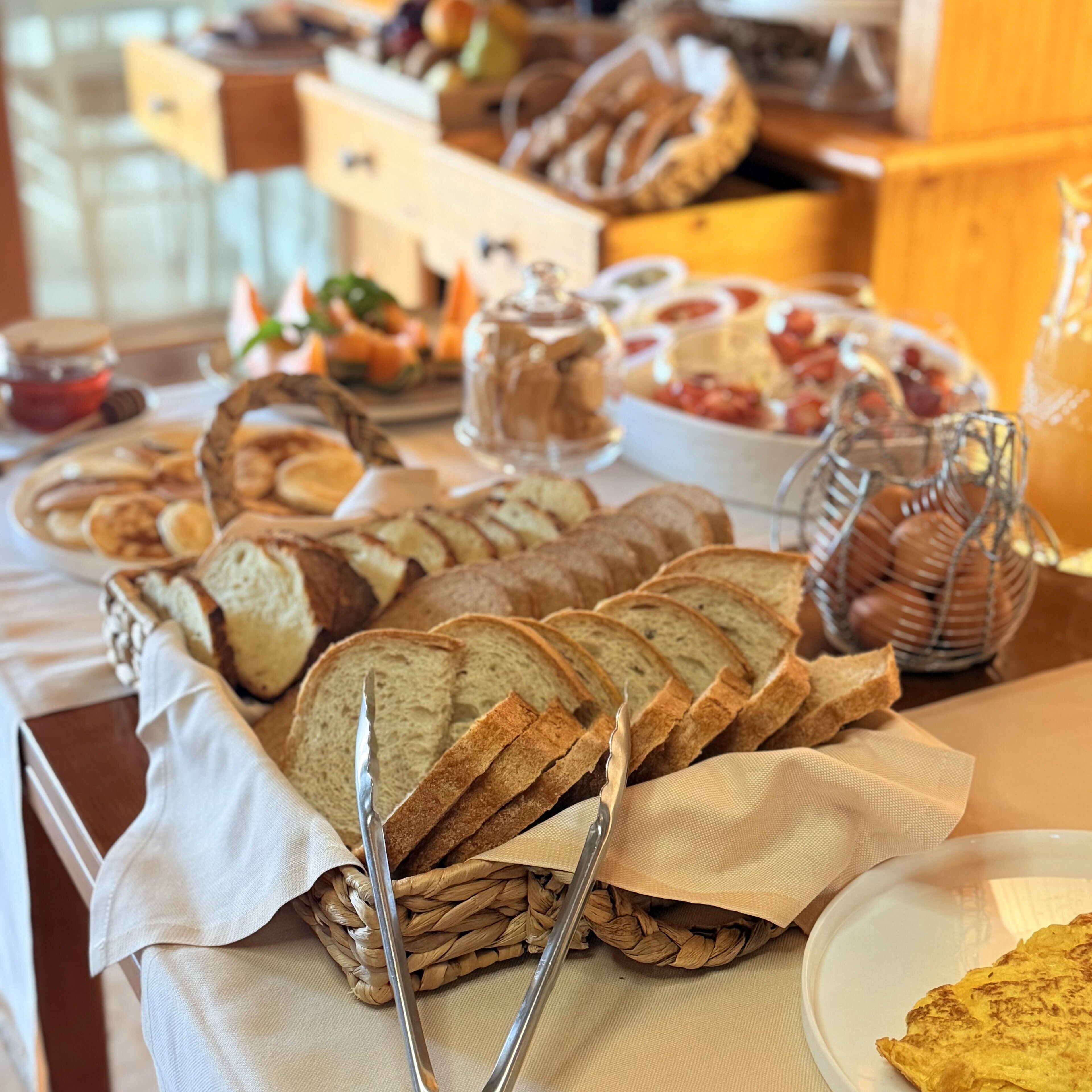Una mesa de buffet con diversos alimentos, incluyendo pan, pasteles y un bol de fruta.