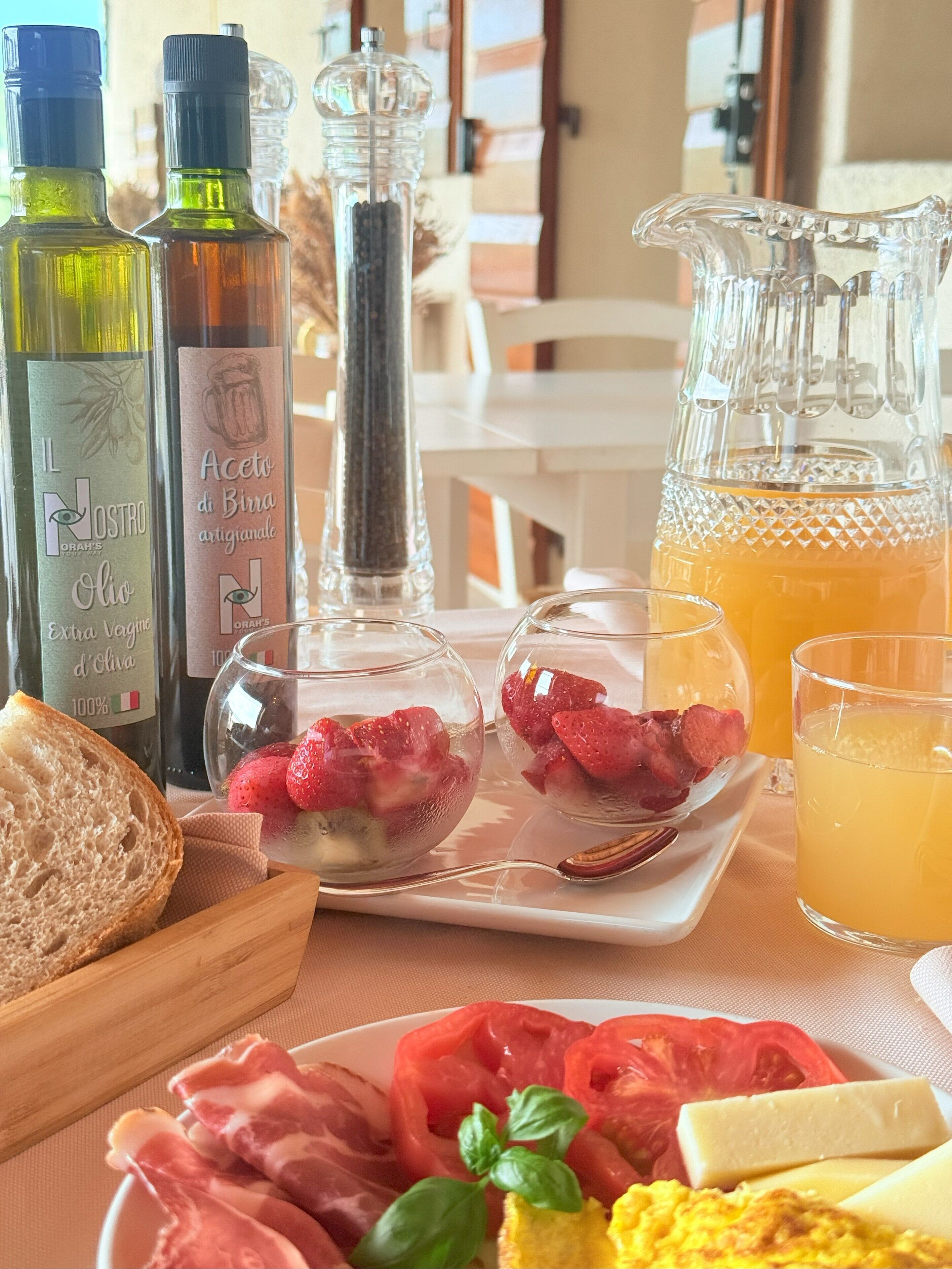 Ein Frühstückstisch mit verschiedenen Speisen und Getränken, darunter Brot, Erdbeeren, Käse und ein Krug Orangensaft.