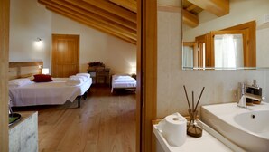 Une chambre avec deux lits, un plafond en bois, un bureau et une salle de bain avec un lavabo et un miroir.
