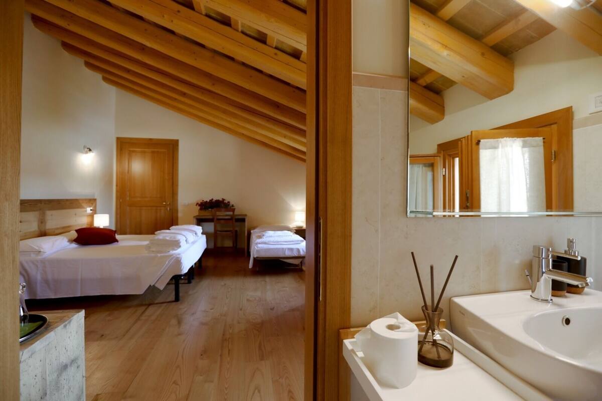 Un dormitorio con dos camas, techo de madera, escritorio y baño con lavamanos y espejo.