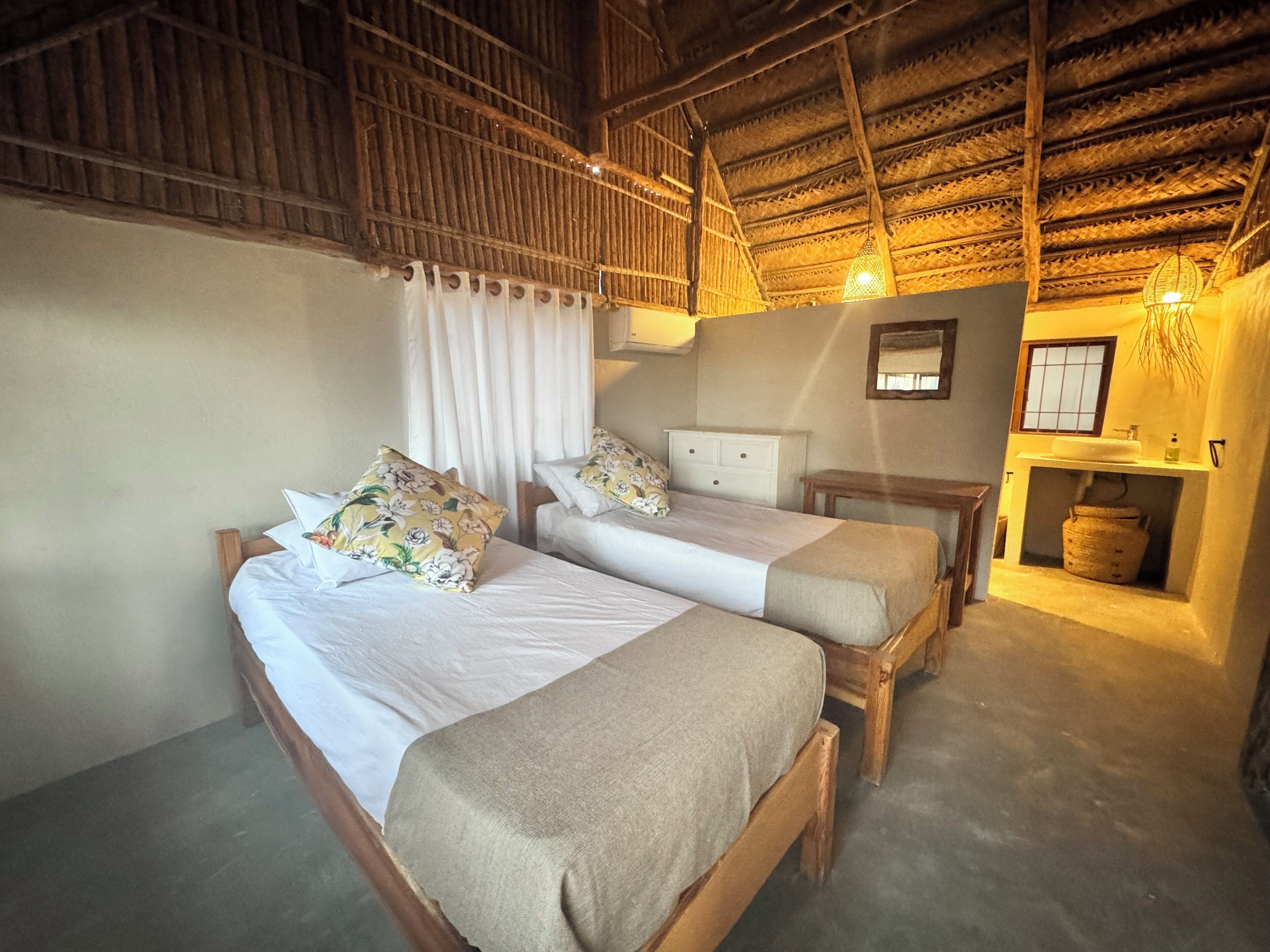 A room with two wooden beds, a small bedside table, a wall-mounted mirror, and a built-in sink with a hanging basket.
