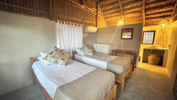 A room with two wooden beds, a small bedside table, a wall-mounted mirror, and a built-in sink with a hanging basket.