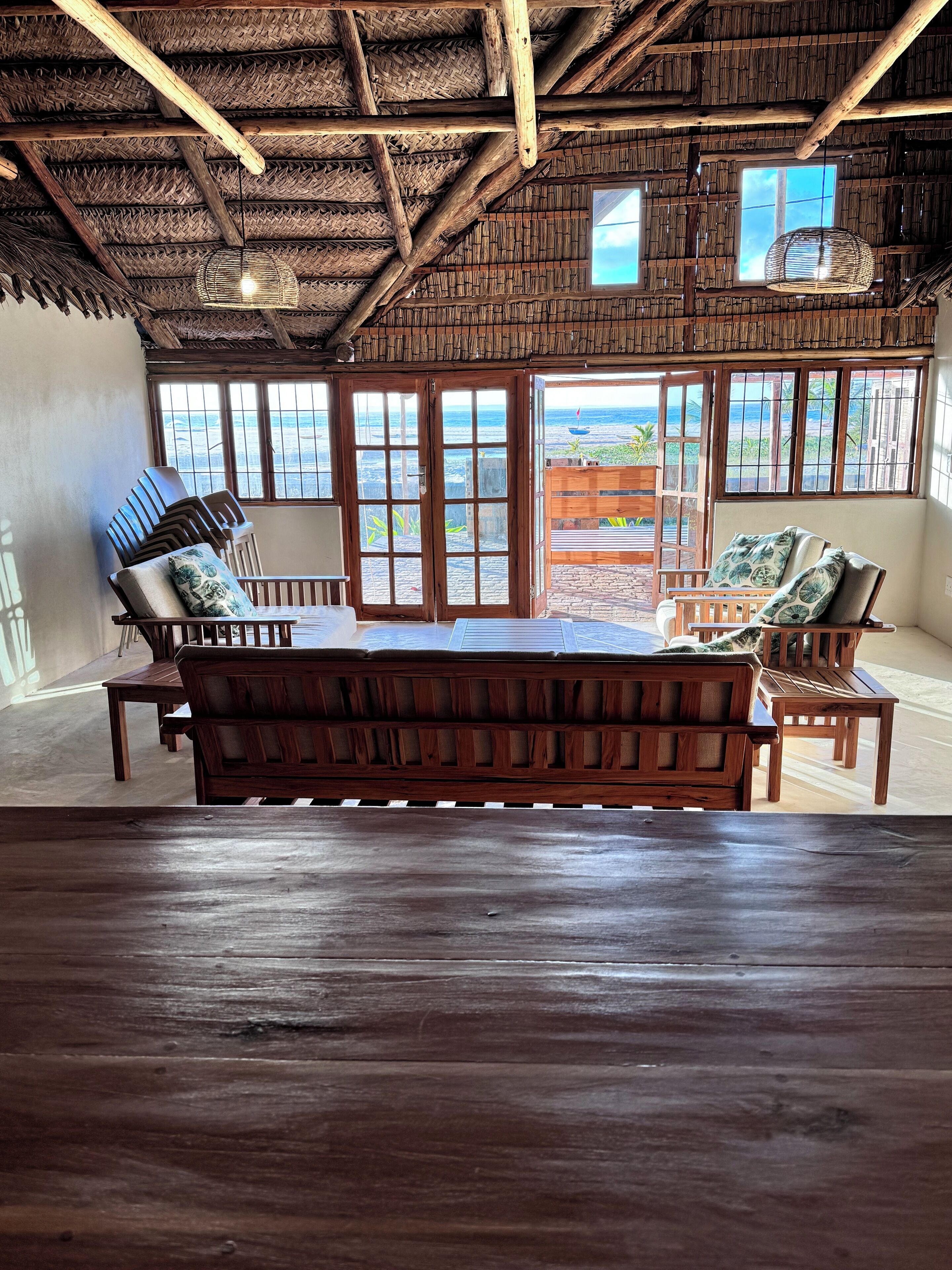 Une pièce avec un banc en bois, une table en bois et une vue sur l’océan grâce à de grandes fenêtres.