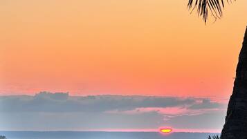 Escena de playa con atardecer, barcos y gente.