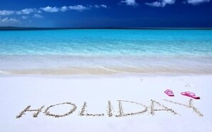 A beach with the word "HOLIDAY" written in the sand and two pink flip-flops placed nearby. - Villa Palmeira (Inhambane)