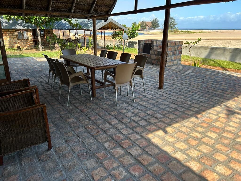 Un patio al aire libre con una mesa y sillas de madera, piso de ladrillo y vista a la playa.