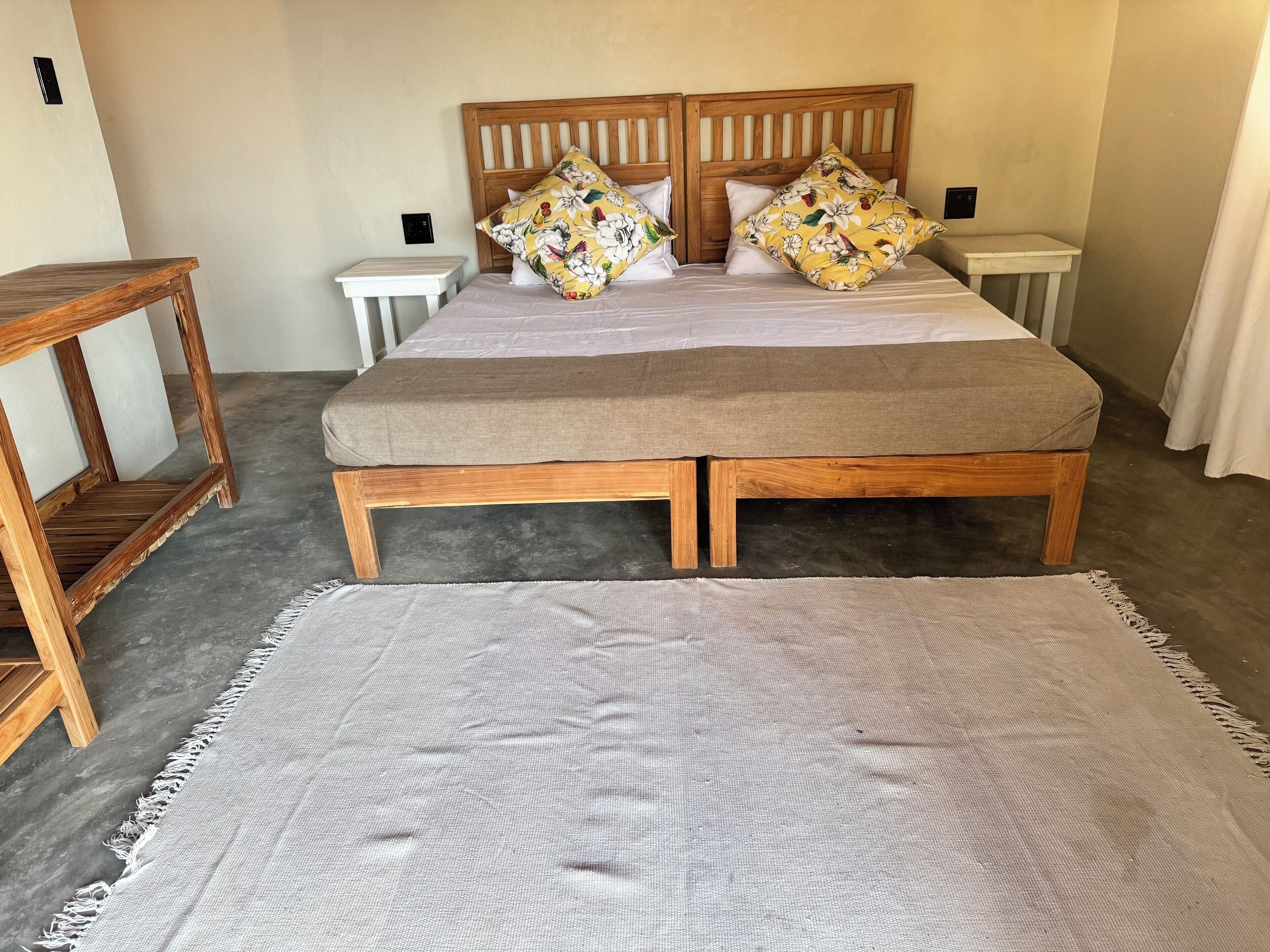 Ein Doppelbett mit Holzvorhang, zwei Nachttische, ein grauer Teppich und ein kleiner Holztisch.