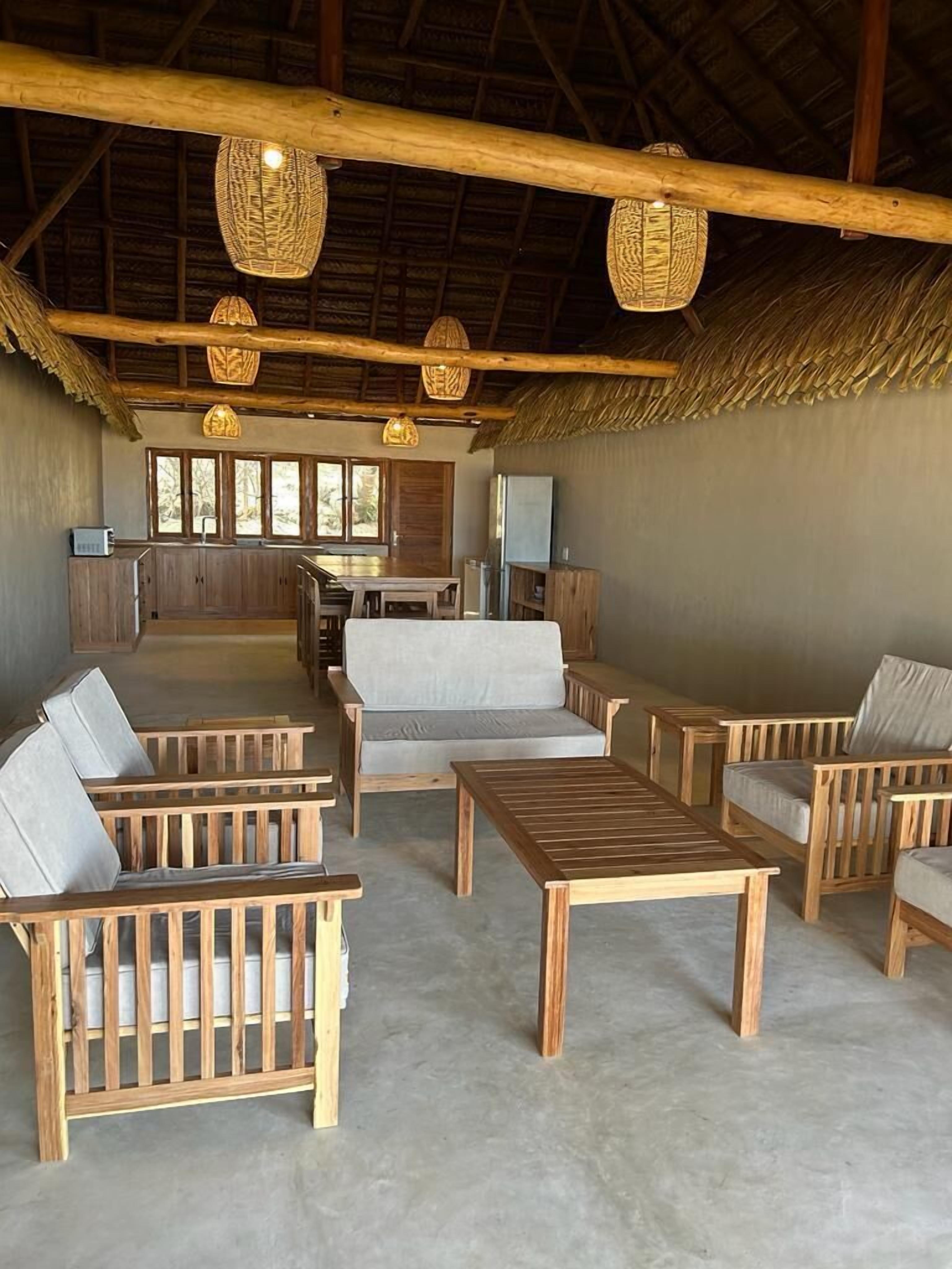 A spacious indoor area with wooden furniture, a thatched roof, and hanging light fixtures.