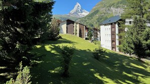 A residential area with modern buildings, a grassy slope, and a mountain peak in the background. - Cervino (Zermatt)